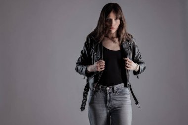 Siyah deri ceket ve gri arka planda kot giyen genç bir kadının stüdyo moda portresi. Bu görüntü güzellik ve moda kavramları için uygundur..