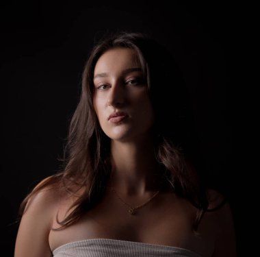 Esmer, güzel bir kadının stüdyo portresi. Doğal makyajı ve koyu arkaplanda altın bir kolyesi var. Bu görüntü moda ve güzellik kavramları için uygundur..