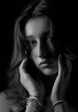 Güzel bir genç kadının tek renkli stüdyo portresi. Elleri nazikçe arka planda ona dokunuyor. Bu görüntü moda güzelliği ve reklam kampanyaları için uygundur..