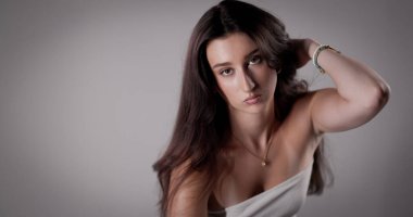 Uzun saçlı, beyaz bluzlu ve gri arka planda mücevherleri olan güzel esmer bir kadının stüdyo portresi. Bu görüntü moda ve güzellik kavramları için uygundur..