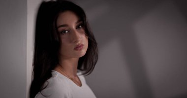 Stüdyo portresi, uzun saçlı, doğal makyajlı ve duvara yaslanmış güzel bir esmer kadın. Bu görüntü moda ve güzellik kavramları için kullanılabilir..