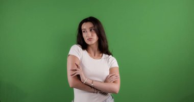 Beyaz tişörtlü esmer bir kadının stüdyo portresi. Kolları yeşil perdeye çarpıştı. Bu görüntü moda güzelliği ve ticari projeler için uygundur..