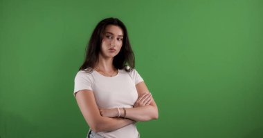 Kollarını kavuşturmuş esmer bir kadının, yeşil bir arka planda çekilmiş stüdyo portresi. Bu görüntü moda güzelliği ve yaşam tarzı projeleri için uygundur..