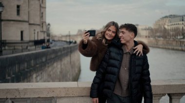 Romantik bir çift Paris 'te cep telefonuyla selfie çekiyor. Fransa' da Seine nehri ve arkasında mimarisi olan. Tatil tatillerinin tadını çıkarıyorlar..
