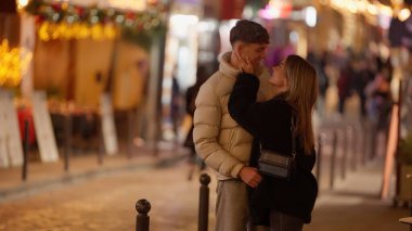 Romantik bir çift gece Paris 'te bir sokakta kucaklaşır. Sahne, Noel ışıklarıyla aydınlatılır ve bokeh seyahat ve sevgililer günü kavramları için sıcak ve davetkar bir ortam yaratır..