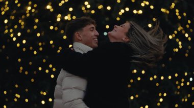 Paris 'te romantik bir çift Noel ışıklarının arka planıyla sarılıyor genç aşıklar sarılıyor ve gülümsüyor tatil sezonunda romantizm ve sevgi gösterisi yapıyorlar..