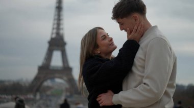 Paris 'te Eyfel Kulesi' nin arka planında genç bir çift sevgiyle sarılıyor. Bu resim seyahat turizmi romantizmi ve ilişki kavramları için uygundur..