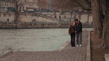 Romantik bir çift Paris 'teki Seine Nehri kıyısında yürüyor. Fransa' da birlikte vakit geçiriyorlar ve kucaklaşıyorlar. Bu resim seyahat turizmi ve yaşam tarzı içeriği için uygundur.