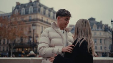 Romantik bir çift Paris 'te arka planda şehir binalarıyla sarılıyor. Aşık genç adam ve kadın şehir ortamında birlikte vakit geçiriyorlar..