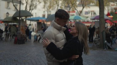 Romantik bir çift Montmartre Paris Fransa 'da bir kaldırım taşı sokağıyla ve arka planda sonbahar sezonu boyunca market tezgahlarıyla kucaklaşıyor. Bu resim seyahat romantizmini ve Avrupa kültürünü resmetmek için kullanılabilir.