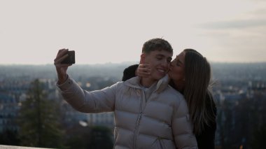 Romantik bir çift Paris 'te bir cep telefonuyla selfie çekiyor Fransa' da şehir manzarası olan kadın, sevgi ve şefkat gösteren erkeği öpüyor..