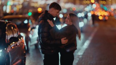 Romantik bir çift, Paris 'te bir şehir caddesinde sarılıyor. Fransa' nın etrafı bokeh ışıkları ve arabalarla çevrili. Bu resim Sevgililer Günü kutlamaları, turizm ve seyahat içeriği için kullanılabilir.