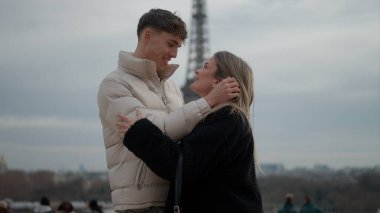 Paris 'te Eyfel Kulesi' nin arka planında genç bir çift sevgiyle sarılıyor. Bu görüntü seyahat turizmi ve romantik temalar için uygundur.
