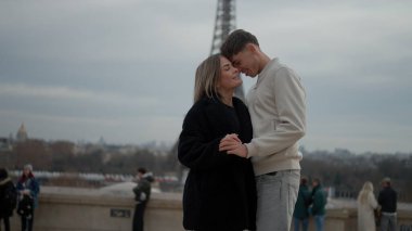 Arka planda Eyfel Kulesi ile Paris 'te romantik bir çift kucaklaşıyor. Genç aşıklar bu popüler Avrupa' da el ele tatillerinin ve şehirlerinin tadını çıkarıyorlar..
