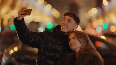 Romantik bir çift gece Paris 'te arka planda Bokeh ışıkları olan akıllı bir telefonla selfie çeker. Bu resim, Avrupa 'da aşk seyahatleri ve kentsel yaşam tarzı kavramlarını göstermek için mükemmeldir..
