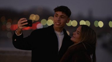 Romantik bir çift gece Paris 'te arka planda Bokeh ışıkları olan akıllı bir telefonla selfie çeker. Bu resim aşk bağlantısını ve kentsel seyahat fotoğrafçılığını iletir.