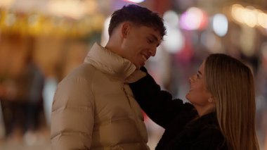 Paris 'teki genç bir çift kış mevsiminde arka planda Bokeh ışıkları ile birbirlerine gülümsüyor. Bu resim Sevgililer Günü promosyonları veya seyahat içeriği için kullanılabilir.