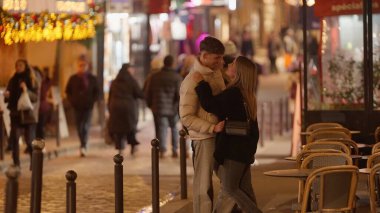 Romantik bir çift, Paris 'te bir sokakta, masalar ve şenlikli Noel ışıklarıyla sarılır. Bu görüntü, Fransa 'nın kalbinde seyahat yaşam tarzı ve tatil temaları için uygun sevgi ve bağlantının özünü yakalar..