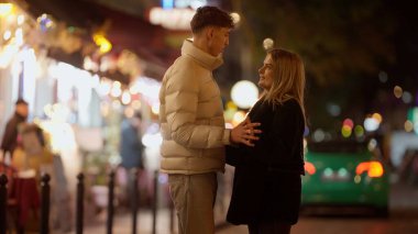 Romantik bir çift gece Paris 'te bir caddede duruyor genç adam ve kadın el ele tutuşuyor ve birbirlerine sevgi ile bakıyorlar seyahat ve romantizm teması için mükemmel bokeh ışıklarıyla çevrili..