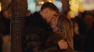 Genç bir çift, gece Paris 'te tutkuyla öpüşüyor. Bokeh ışıkları ve süslü bir sokak lambasıyla aydınlatılıyor. Resim, bir kutlama sırasında aşkı ve şehir hayatını anlatıyor..