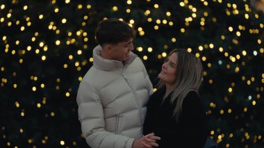 Paris 'te romantik bir çift Noel ışıklarının güzel arka planıyla sarılıyor. Genç adam ve kadın, şehirde kış tatilinin tadını çıkarıyorlar..