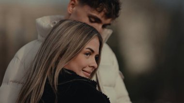 Paris 'te genç bir kadınla romantik bir çift görülüyor. Bir erkek onu arkadan kucaklarken gülümsüyor. Bu resim seyahat yaşam tarzı ve ilişki bağlamlarında ticari kullanım için sevgi ve birlikteliği taşır.