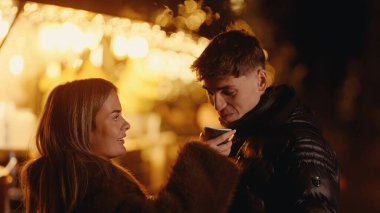 Romantik bir çift, Paris 'teki bir Noel pazarında kahve içiyor. Etrafı bokeh ışıklarıyla çevrili. Kışlık paltolar giyiyorlar, kürk giyiyorlar ve aşkı kutluyorlar..