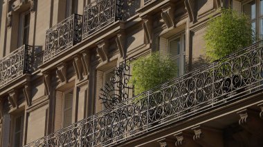 Fransa 'da bir Paris binasının dış tarafında süslü demirler ve yeşil bitkilerle dolu balkonlar var. Bu resim Avrupa turizmini veya kentsel yaşamı temsil etmek için kullanılabilir..