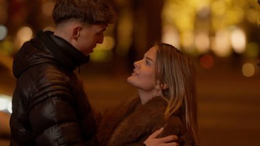 Geceleri Paris 'te birbirine aşık genç bir çift arka planda Bokeh ışıkları ile sarılıyor. Bu resim seyahat romantizmi ve ilişki temaları için uygundur.