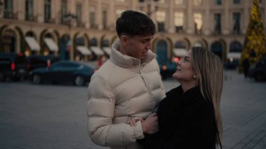 Paris 'te romantik bir çift, şehir manzarasının ortasında sevgi ve şefkat sergiliyor. Gece boyunca binalar ve bir Noel ağacı ile. Bu resim seyahat yaşam tarzı ve ilişki içeriği için kullanılabilir.