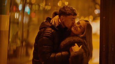 Genç bir çift Paris 'te geceleri sarılıp öpüşüyor. Sıcak ışıklandırma ve şehir arkaplanı Sevgililer Günü içeriği için mükemmel romantik bir ortam yaratıyor..