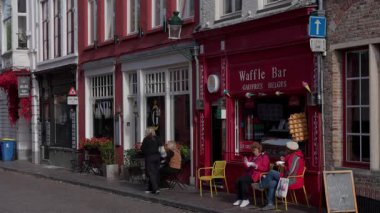 BRUGES, BELGIUM - 15 Eylül 2025 - Bruges 'deki renkli bir kafede waffle ve kahve içen insanların sokak manzarası