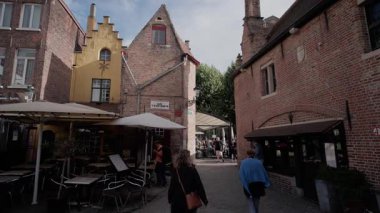 BRUGES, BELGIUM - 15 Eylül 2025 - Turistler tarihi Bruges mimarisi ile çevrili dar bir kaldırım taşı caddesinde yürüyorlar