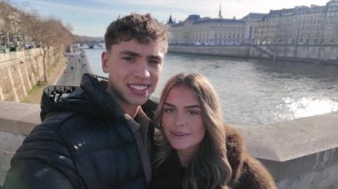 Aşık bir çift, arka planda Seine Nehri ve Paris mimarisi ile Paris 'te gizli selfie çekiyor. El kamerası, romantik sosyal medya içerikli seyahat videolarını ya da promosyon materyallerini yakalıyor..