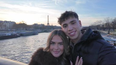 Aşık genç bir çift, Paris 'te arka planda Eyfel Kulesi olan Pov selfie' lerini çekiyor. Nehrin üzerinde duruyor ve sosyal medya içeriğine gülümsüyorlar..