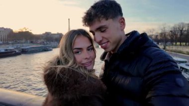 Genç bir çift Paris 'te bir köprüde gizli selfie çekiyor. Eyfel Kulesi arka planda Seine Nehri' nin ağaç ve binaları ile birlikte görünüyor..