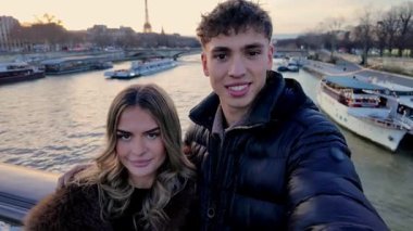 Aşık bir çift, Paris 'teki Seine Nehri' nin üzerindeki bir köprüde gizli selfie çekiyor. Eyfel Kulesi arka planda görünüyor. Video, el bilgisayarı tarzı sosyal medya içerikli seyahat videolarında veya romantik kaçamaklarda çekiliyor..