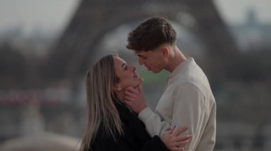 Paris 'te arka planda Eyfel Kulesi' yle romantik bir çift öpüşür. El kamerası onların sevgi dolu kucaklamalarını yakalar. Yumuşak odak noktası samimi anı daha da yakınlaştırır..
