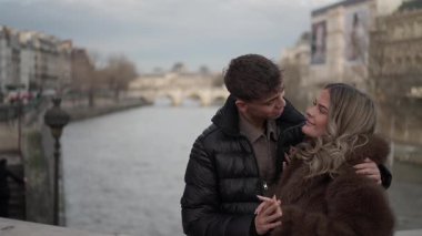 Genç bir çift Paris 'te Seine nehri ve arka planda köprüler ile kucaklaşıyor. Aşıklar Avrupa' da birlikte vakit geçiriyorlar ve bir seyahat ve aşk konsepti sergiliyorlar..