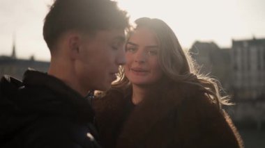 Paris 'te gün batımının keyfini çıkaran genç bir çiftin yakın çekimi. Arka planda, erkek ve kadın gülümseyip mutlu görünürken şehrin ufuk çizgisi görülüyor..