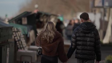 Bir çift Paris 'teki Seine Nehri' nde yürürken el ele tutuşuyor. Arka manzara, güneşli bir günde el kamerasıyla çekilen kitap tezgahlarının yanında gezinen genç aşıkları gösteriyor..