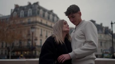 Paris 'te sevgi dolu bir çift, arka planda görünen klasik Paris mimarisi ile kucaklaşır. Sahne, romantik bir seyahat ve Avrupa şehir yaşam tarzını aktarır..