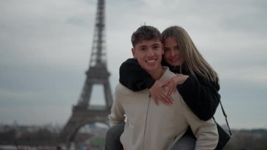 Genç bir çift, arka planda Eyfel Kulesi 'yle Paris' te sırtüstü gezmekten zevk alır. Adam kadını sırtüstü taşır ve gülümseyip poz verir. Avrupa 'nın ikonik şehrinde romantik bir anı yakalar..