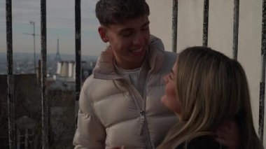 Genç bir çift Paris 'te bir çatıda sarılıyor. Arka planda Eyfel Kulesi var. Kadın ve erkek birbirlerine sevgi ve sevgiyle bakıyorlar..