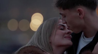 Paris 'te gece Fransa' yı kucaklayan sevgi dolu bir çiftin yakın plan çekimi arka planda romantik ve samimi bir atmosfer yaratan yumuşak bokeh ışıkları yer alıyor..