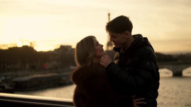 Romantik bir çift, Paris 'te arka planda Eyfel Kulesi' ne sarılır. Gün batımında Fransa 'da altın saat ışığı sıcak ve sevgi dolu bir atmosfer yaratır..