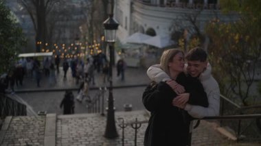 Romantik bir çift Montmartre Paris 'te sarılır kadın adamı yanağından öper arka plan bulanıklaşır Sacre-Coeur bazilikasını ve hareketli bir sokak sahnesini gösterir.