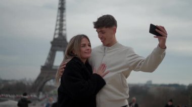 Bir çift Paris 'te arka planda Eyfel Kulesi ile selfie çekiyor. Sahne, seyahat ve turizm deneyimleri sırasında romantik bir aşk ve birliktelik anı yakalıyor..