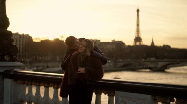Romantik bir çift, Paris 'teki Alexandre III Köprüsü' nde altın bir günbatımı sırasında arka planda Eiffel Kulesi, ışık şehrindeki sevgi ve sevgiyi simgeliyor.