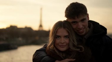 Paris 'te genç bir çift, gün batımında arka planda Eyfel Kulesi görünür bir şekilde Paris şehrine karşı sevgi ve beraberlik sergiliyor.